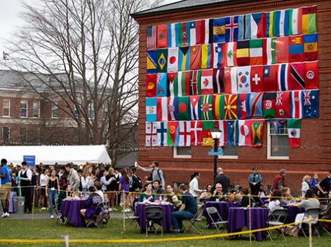 Students eating at tables outside under a wall of world flags