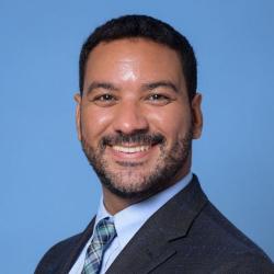 Jean-Robert smiling in a suit against a blue background